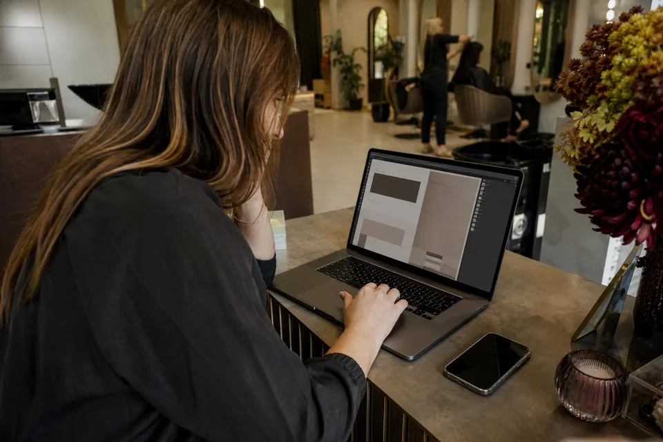 Właścicielka salonu edytuje firmową stronę internetową na laptopie przy recepcji